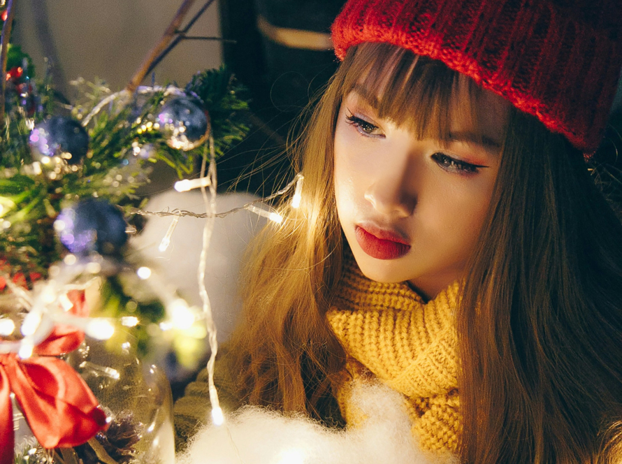a girl looks somber staring at her Christmas tree, representing holiday loneliness