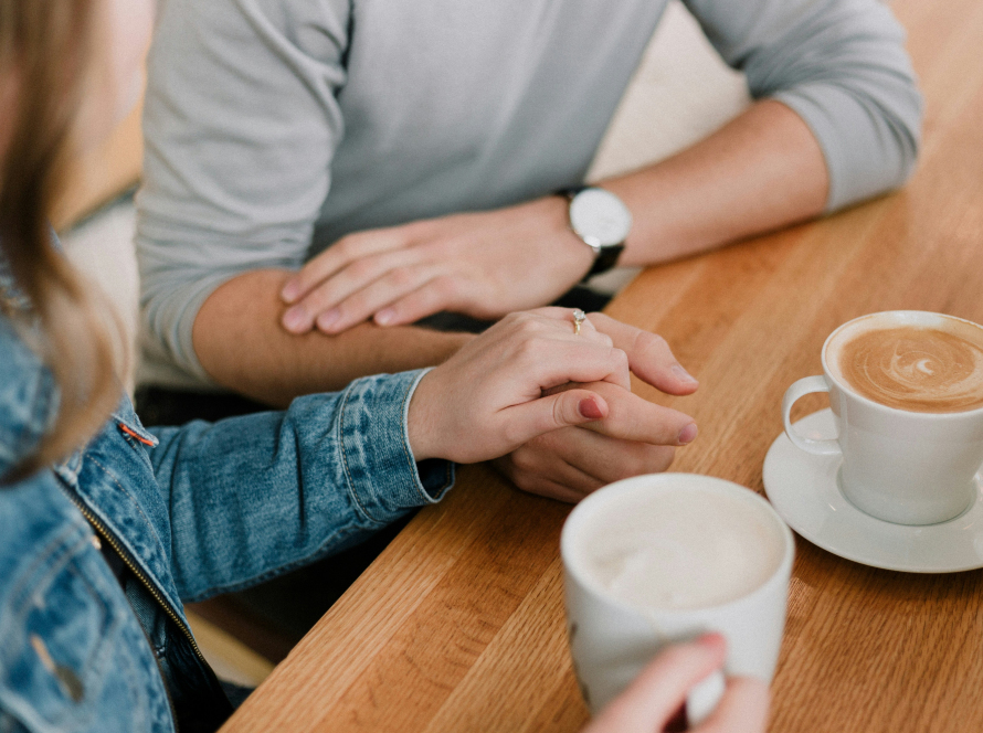 a couple holds hands at a table while drinking coffee, a representation of healthy relationships