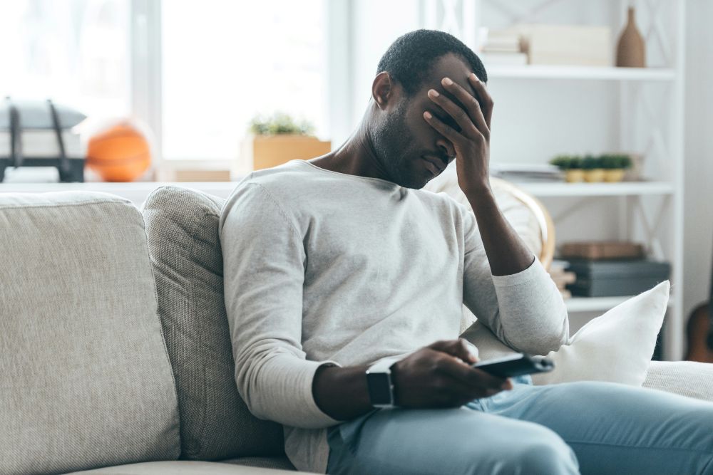 Man lays his head in his hand while changing channels on the TV. Contemplates trauma therapy.