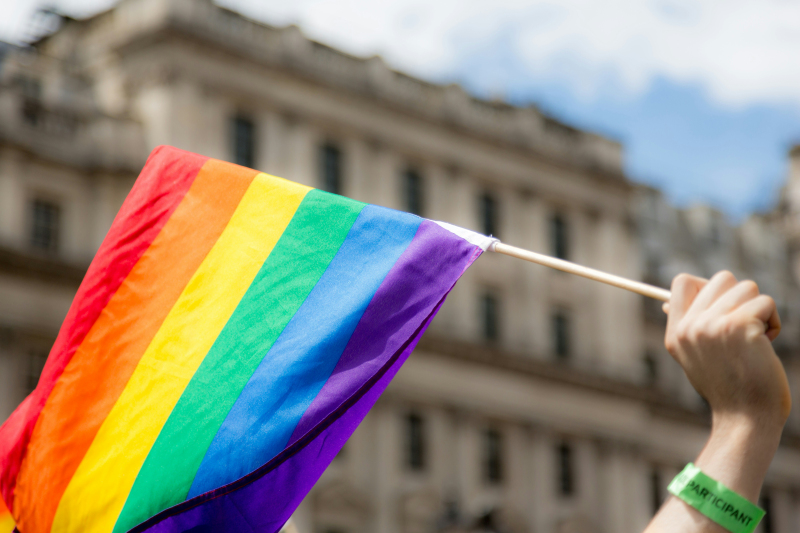 A hand holds up a rainbow flag in support of the LGBTQIA+ community