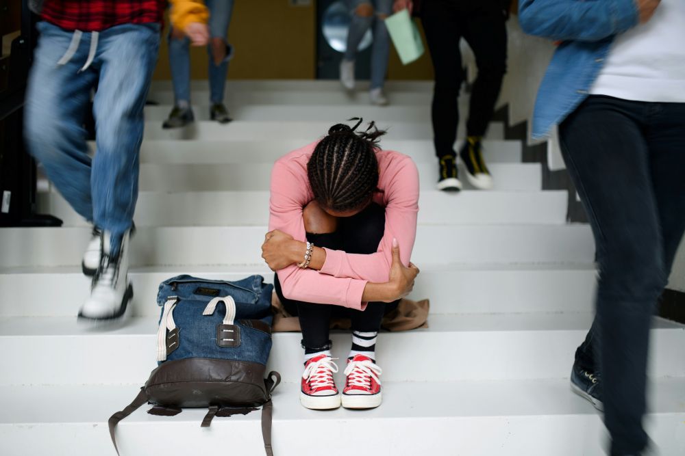 Older Teenager bends over in grief while sitting on high school steps in need of Trauma therapy