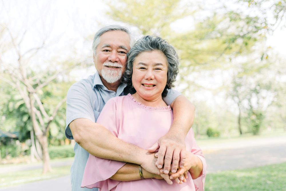 Older Asian couple hugs each other for posed photo as they celebrate long lasting relationship.