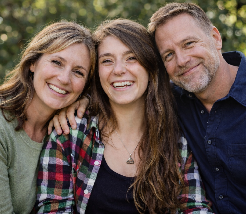Older teenage daughter sits between happy mother and father with a close family bond after receiving family Therapy at Brickel & Associates